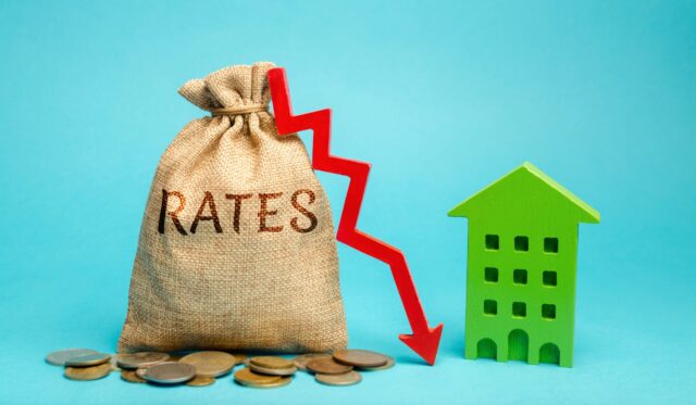 Money bag with the word Rates, down arrow and wooden house. The concept of reducing interest rates on mortgages. Low interest rates on housing loans. Real estate market and loan.